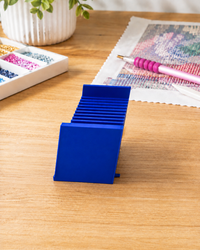 Blue 3D printed 12-slot tilted drill packet tray on a craft table beside a diamond painting canvas – image 4