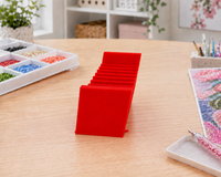 Red 3D printed 12-slot tilted drill packet tray on a craft table with a drill storage box – image 3