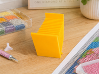 Yellow 3D printed 12-slot tilted drill packet tray on a craft table with drill pens and a storage box – image 5