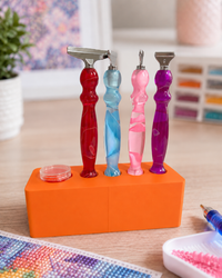 Orange Drill Pen Station holding four resin drill pens, with wax in the wax well, on a craft table – image 15